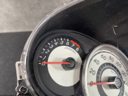 Close-up of a car instrument cluster showing a tachometer and speedometer, with red needles resting near zero at idle, highlighting the rpm and speed scales.