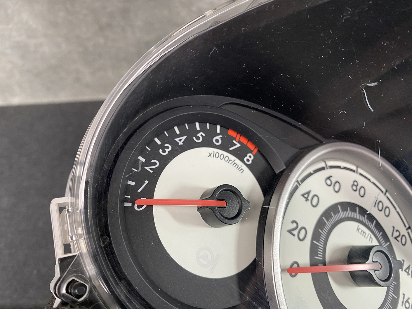 B477_10 MAZDA DEMIO MAZDA 2 DE3FS Genuine Instrument Cluster D01J55430 K9001 » NZ.95 » JDM-PARTS NZ » JDM-PARTS NZ Close-up of a car instrument cluster showing a tachometer and speedometer, with red needles resting near zero at idle, highlighting the rpm and speed scales. MAZDA DEMIO MAZDA 2 DE3FS Genuine Instrument Cluster D01J55430 K9001 » JDM-PARTS NZ