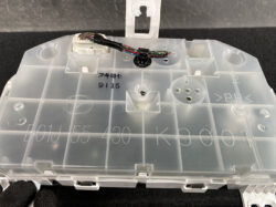 Translucent plastic electronics module with a white connector and a bundle of colored wires (red, blue, green, brown) plugged into it, mounted on the housing surface.
