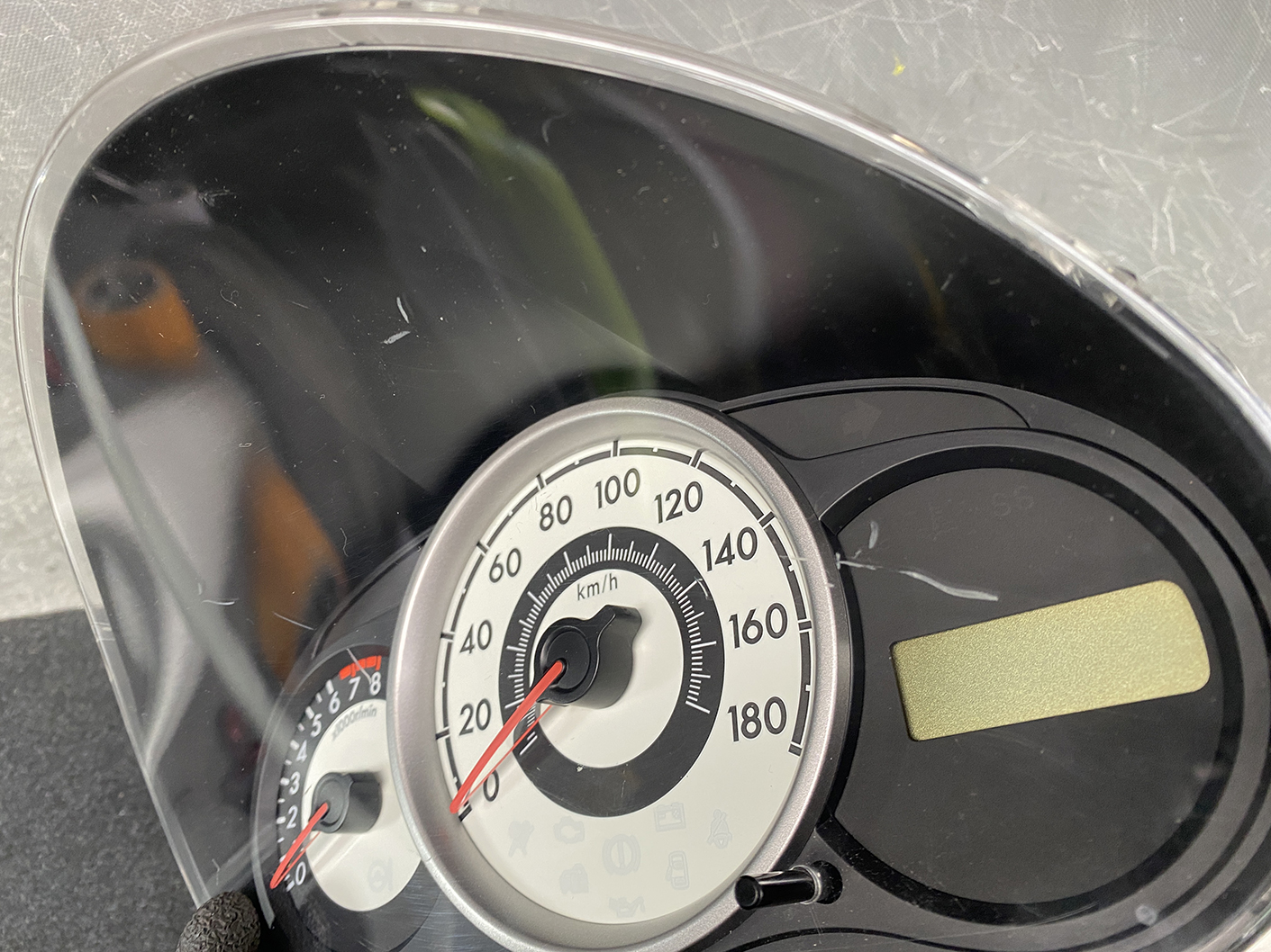 B477_9 MAZDA DEMIO MAZDA 2 DE3FS Genuine Instrument Cluster D01J55430 K9001 » NZ.95 » JDM-PARTS NZ » JDM-PARTS NZ Close-up of a car speedometer showing 0–180 km/h with the red needle near 0. MAZDA DEMIO MAZDA 2 DE3FS Genuine Instrument Cluster D01J55430 K9001 » JDM-PARTS NZ