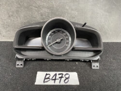Circular car speedometer displaying 0–180 km/h inside a black plastic housing on a grey surface.