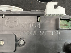 Close-up of a car electronic control unit housing with a Mazda logo and part numbers K1054 D09M 55 430, exposing a small circuit board edge.