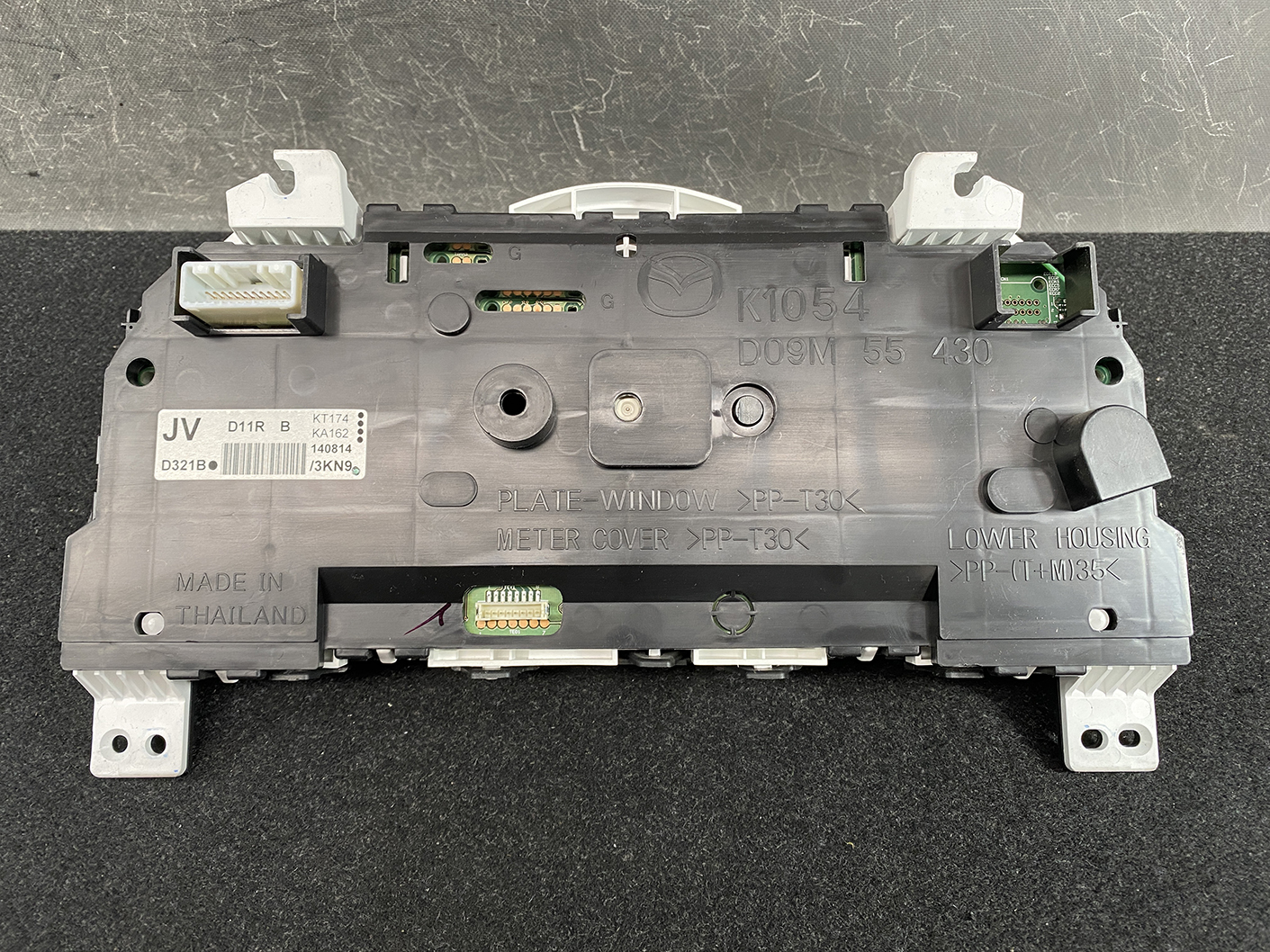 B478_6 MAZDA DEMIO CX-3 Genuine Instrument Cluster K1054 / D09M 55 430 » NZ1.95 » JDM-PARTS NZ » JDM-PARTS NZ Back view of a car instrument cluster module with multiple connectors and a textured gray plastic housing, showing mounting points and label markings like K1054 and D09M 55 430. MAZDA DEMIO CX-3 Genuine Instrument Cluster K1054 / D09M 55 430 » JDM-PARTS NZ