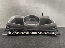 Automotive instrument cluster housing with a central circular gauge opening and two side air vent ducts, placed on a workshop table.