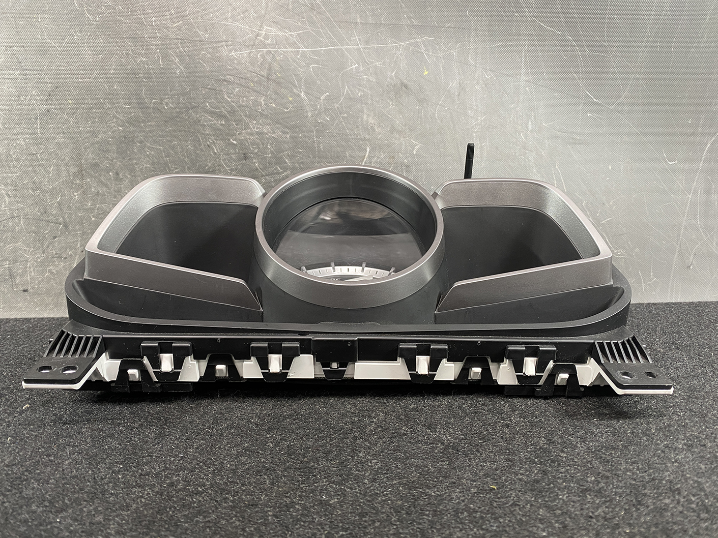 B478_8 MAZDA DEMIO CX-3 Genuine Instrument Cluster K1054 / D09M 55 430 » NZ1.95 » JDM-PARTS NZ » JDM-PARTS NZ Automotive instrument cluster housing with a central circular gauge opening and two side air vent ducts, placed on a workshop table. MAZDA DEMIO CX-3 Genuine Instrument Cluster K1054 / D09M 55 430 » JDM-PARTS NZ
