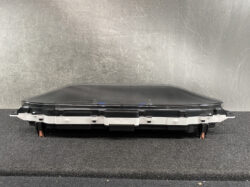 Automotive instrument cluster or dashboard screen module with mounting brackets, resting on a black surface.