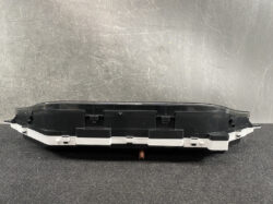 Detached car instrument cluster housing with a clear lens resting on a dark surface, black and white plastic trim visible.