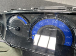 Hybrid car dashboard: blue 0–180 km/h speedometer with a left charge/power gauge and reflective glass glare