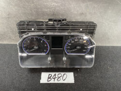 Vehicle instrument cluster with two round gauges (tachometer and speedometer) and a central display, housed in a black plastic dash unit with a clear plastic cover.