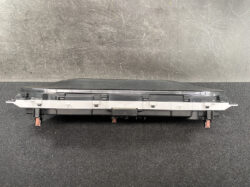 Long black automotive electrical module with orange-red connector latches at both ends and a metal mounting strip along the middle, shown from the side on a dark surface.