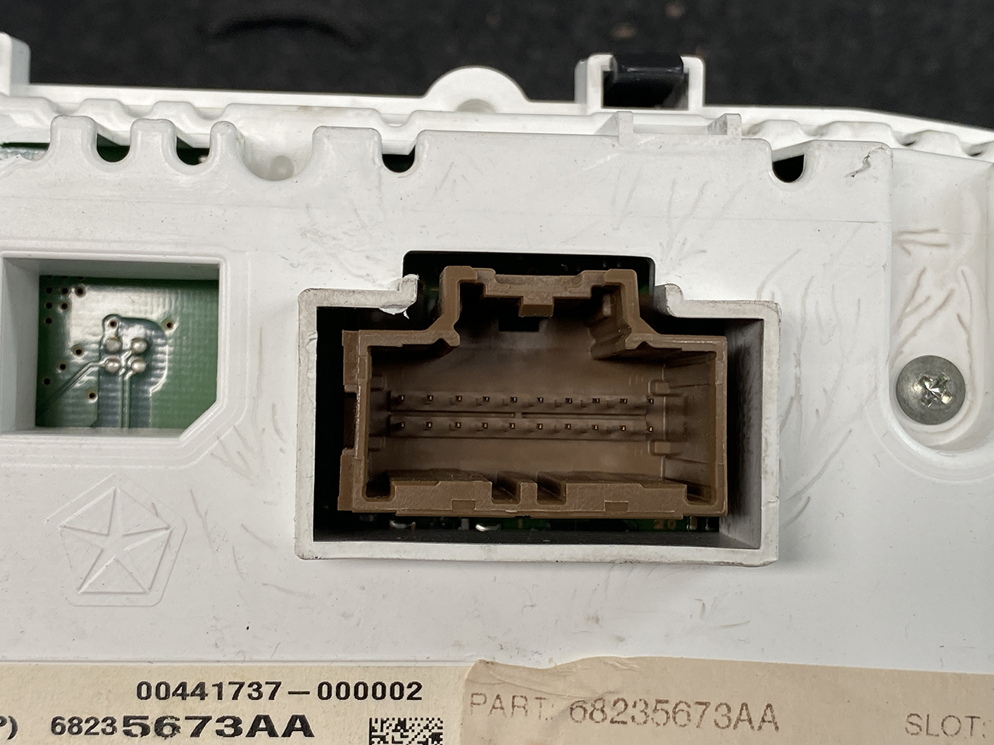 B482_5 Jeep Grand Cherokee WK57A Genuine Instrument Cluster 68235673AA » NZ1.95 » JDM-PARTS NZ » JDM-PARTS NZ Close-up of a brown rectangular multi-pin electrical connector set in a white plastic panel, with a small green circuit board visible on the left. Jeep Grand Cherokee WK57A Genuine Instrument Cluster 68235673AA » JDM-PARTS NZ
