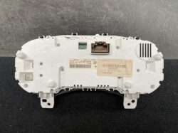 Rear view of a car instrument cluster housing in white plastic, with connector ports and a beige label/stickers nearby.