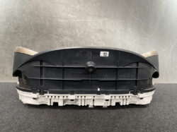 Rear view of an automotive instrument cluster housing with beige trim on the sides, placed on a dark work surface.