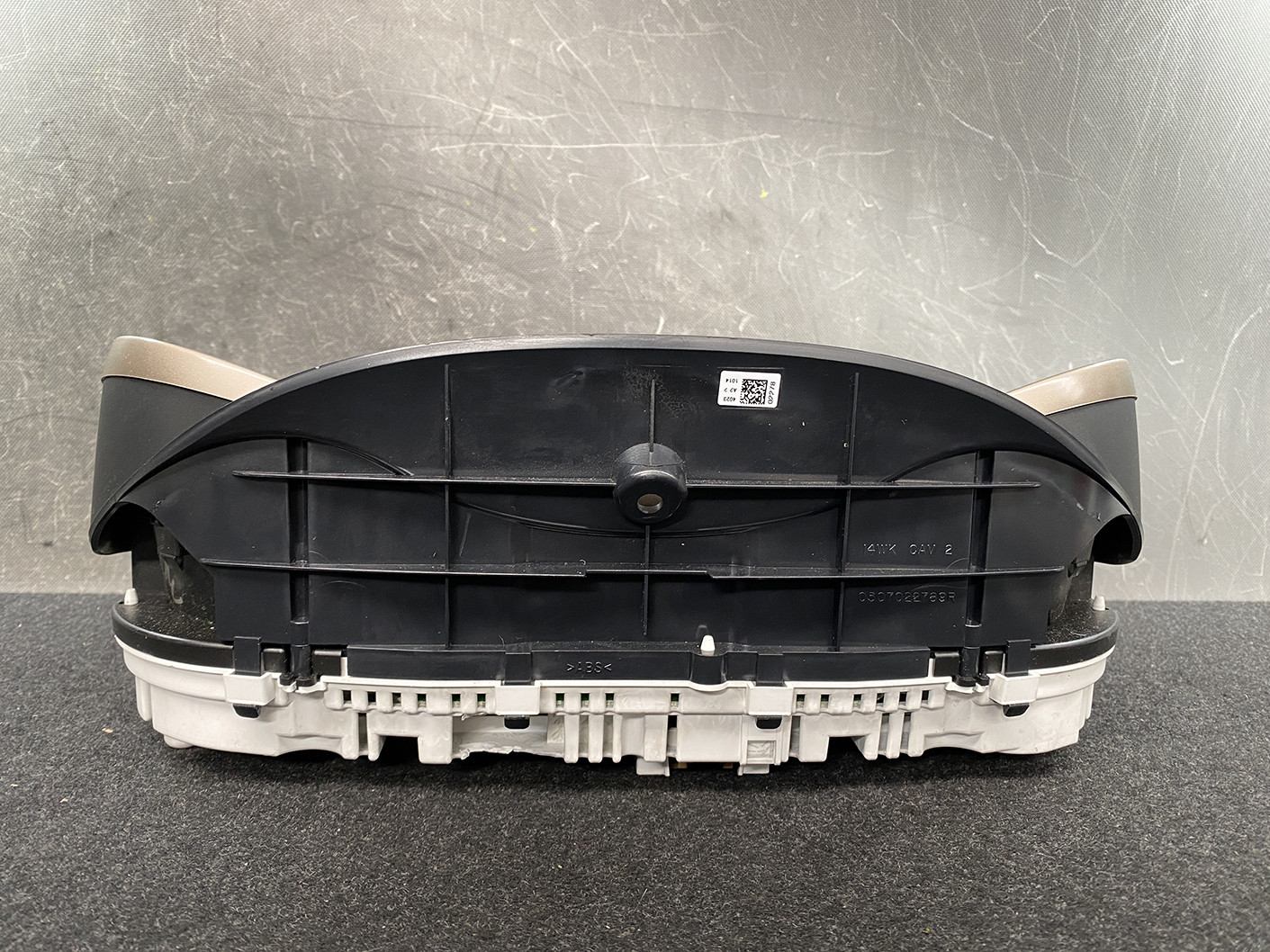 B482_7 Jeep Grand Cherokee WK57A Genuine Instrument Cluster 68235673AA » NZ1.95 » JDM-PARTS NZ » JDM-PARTS NZ Rear view of an automotive instrument cluster housing with beige trim on the sides, placed on a dark work surface. Jeep Grand Cherokee WK57A Genuine Instrument Cluster 68235673AA » JDM-PARTS NZ