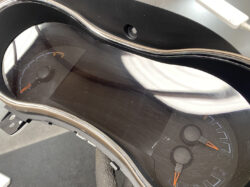 Close-up of a motorcycle instrument cluster with a glossy black cover and orange-tipped needles near zero.