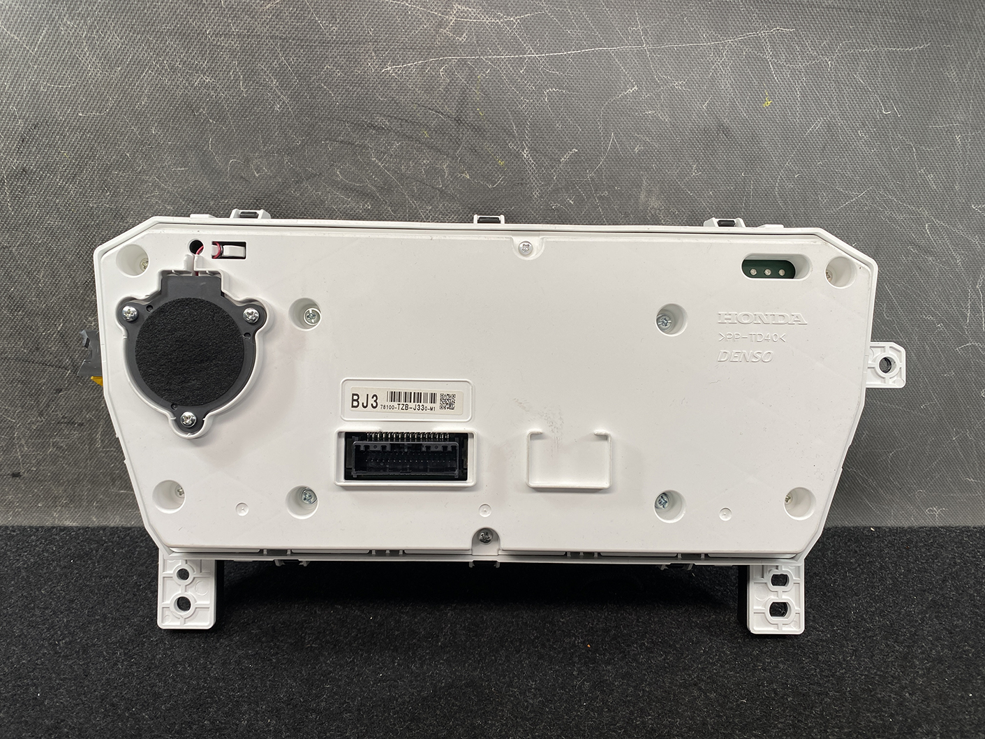 B483_5 HONDA FIT JAZZ GR6 Genuine Instrument Cluster BJ3 78100-TZB-J330-M1 » NZ1.95 » JDM-PARTS NZ » JDM-PARTS NZ Rear view of a white car instrument cluster module showing a large circular black component on the left, with multiple connectors and mounting points nearby. HONDA FIT JAZZ GR6 Genuine Instrument Cluster BJ3 78100-TZB-J330-M1 » JDM-PARTS NZ
