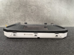Automotive digital instrument cluster with rectangular display in a white housing on a dark work surface.