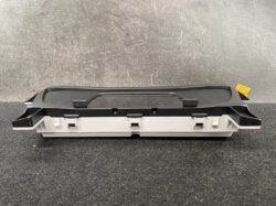 Automotive dashboard control module (center console) with a black cover and gray housing on a dark surface.