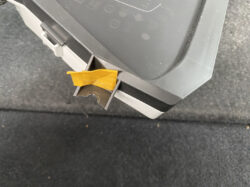 Close-up of a gray plastic panel with an orange tape piece lodged in a small slot, mounted above a dark surface.