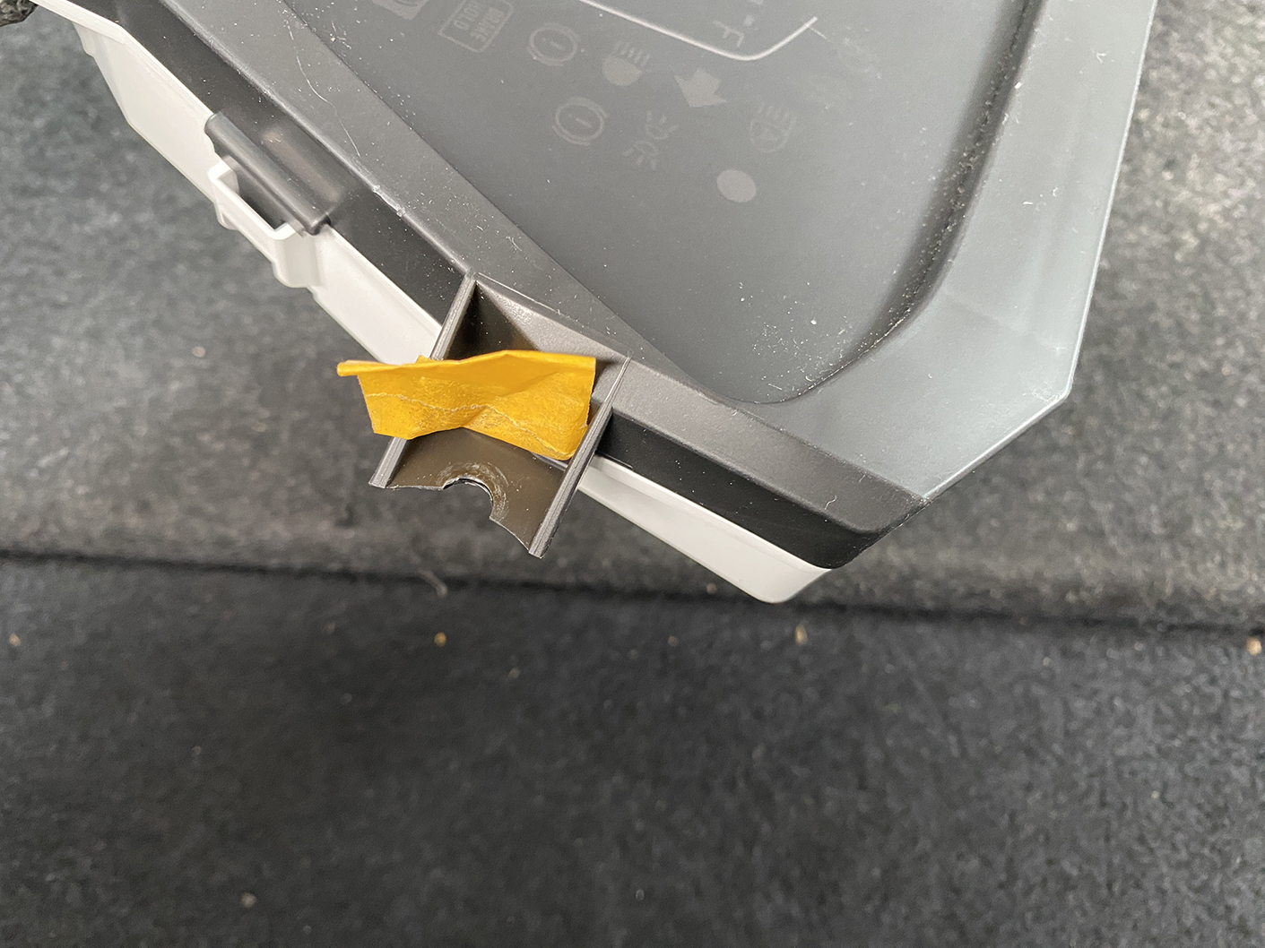 B483_9 HONDA FIT JAZZ GR6 Genuine Instrument Cluster BJ3 78100-TZB-J330-M1 » NZ1.95 » JDM-PARTS NZ » JDM-PARTS NZ Close-up of a gray plastic panel with an orange tape piece lodged in a small slot, mounted above a dark surface. HONDA FIT JAZZ GR6 Genuine Instrument Cluster BJ3 78100-TZB-J330-M1 » JDM-PARTS NZ
