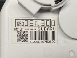 Close-up of a white device label with a barcode, QR code, and 'SUBARU' text on a white automotive part.
