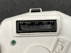 Close-up of a white device showing a wide rectangular multi-pin connector with two rows of small gold pins inside a dark housing; a green indicator light sits nearby.