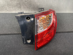 Tail light assembly with red outer lens and clear amber inner section mounted on a dark backing plate on a black surface.