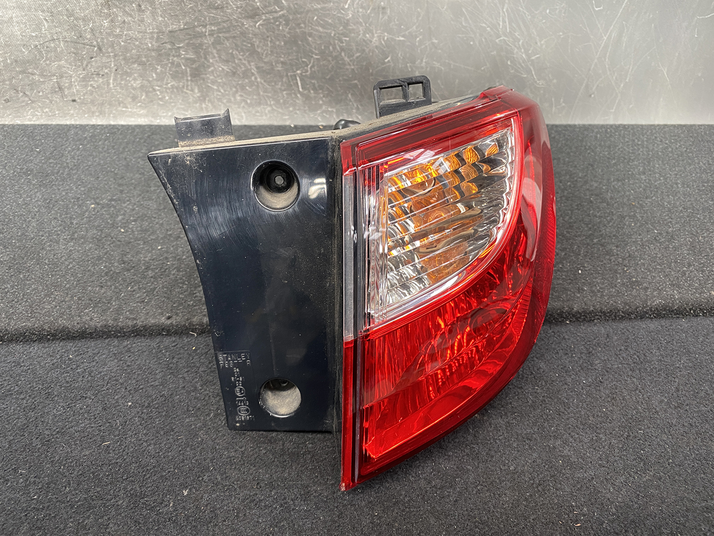 B485_3 MAZDA PREMACY CW NISSAN LAFESTA Taillight P9377 Right Side x1 » NZ1.95 » JDM-PARTS NZ » JDM-PARTS NZ Tail light assembly with red outer lens and clear amber inner section mounted on a dark backing plate on a black surface. MAZDA PREMACY CW NISSAN LAFESTA Taillight P9377 Right Side x1 » JDM-PARTS NZ