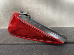 Red automotive tail light assembly with black upper housing, resting on a dark textured surface.