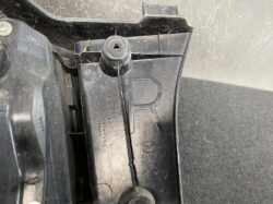 Close-up of a black car component showing '12V' and a circular mounting boss. A Mazda emblem is faintly molded nearby.
