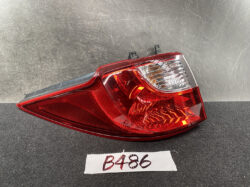 Car tail light assembly with red lens and clear reverse light section on a dark surface.