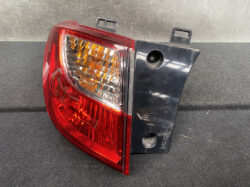 Rear car taillight assembly with red lens and amber reflector, mounted on a black plastic housing with mounting tabs.