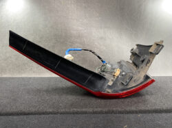 Car tail light assembly with a red lens and black housing, showing exposed wiring and connectors on a workshop surface.