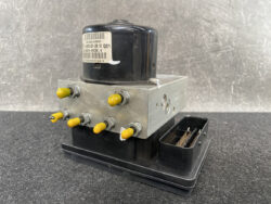 Automotive brake modulator with a metal valve block, yellow port caps, and a black base module.