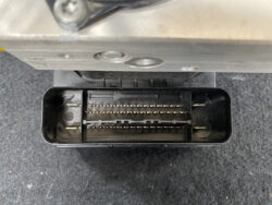 Close-up of a black rectangular automotive connector with two rows of gold pins inside a metal housing.