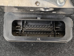 Rectangular multi-pin automotive connector housing with two rows of metal pins, inside a black plastic frame. Used to plug into a control module.
