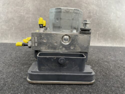 ABS hydraulic control module from a vehicle, with yellow capped hydraulic lines and a metal housing mounted on a base plate