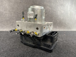 Automotive ABS pump module with metal block and four brake line fittings connected to a black plastic base connector.
