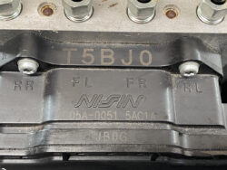 Close-up of a Nissin brake caliper with RR FL FR RL markings and embossed code T5BJO, dusty metal surface and bolts nearby.