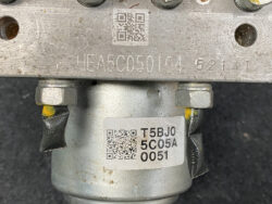 Metal industrial component with stamped code 'HEA5C050104 52141' and a lower label 'T5BJO 5C05A 0051' plus two QR codes and bolts nearby.