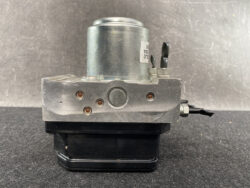 Automotive ABS brake modulator with a silver metal valve block, round motor on top, and side wiring connector on a black base.
