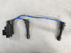 Ignition coil pack with two spark plug wires connected to spark plugs on a gray surface.
