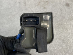 Close-up of a three-pin automotive electrical connector with a locking latch, held by a gloved hand.