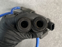 Two black rubber boot ends with hollow centers held by a gloved hand, blue wire in the background.