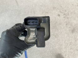 Close-up of a four-pin automotive electrical connector with a locking clip, held by a gloved hand.