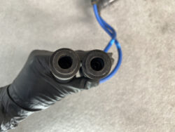 Two black rubber bushings with hollow centers held by a gloved hand, connected to a blue cable.