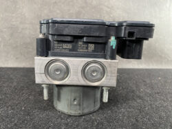 ABS hydraulic control module with twin piston caps and black electronic unit on top side.
