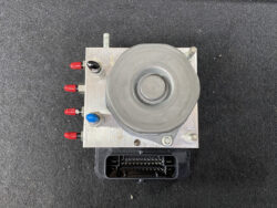 Top view of an automotive ABS brake modulator with hydraulic pump on a metal housing and a multi-pin electrical connector at the bottom.