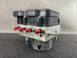 Bosch automotive ABS pump module with a metal valve block, red port caps, and a black control unit on top.