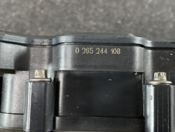 Close-up of a camera body showing the serial number 0 265 244 108 and metal strap hinges/buckles on the sides.